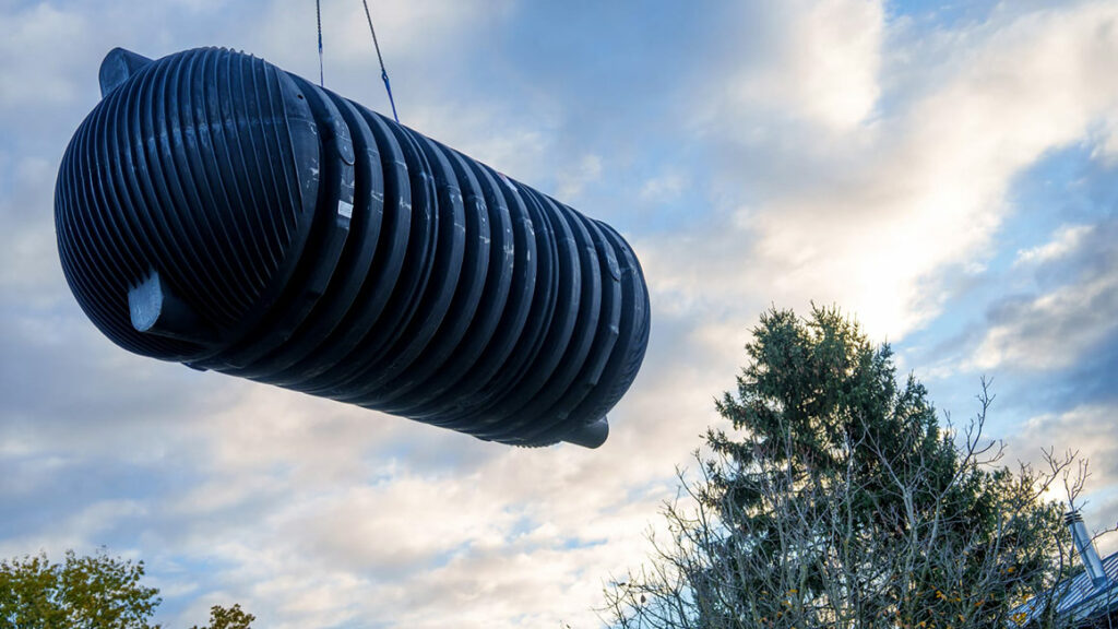 Une citerne de 22 000 litres est soulevée à l'aide d'une grue de chantier dans la fouille préparée à cet effet