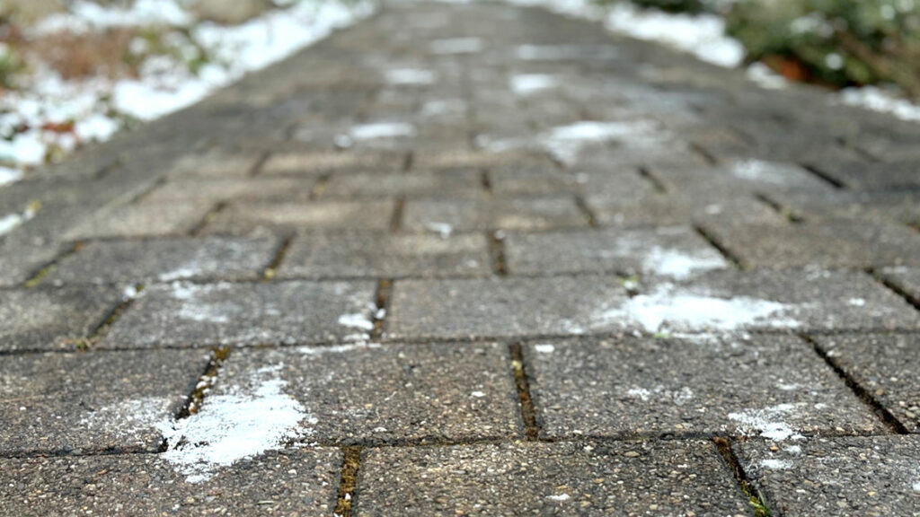 Gehweg mit mehreren Streusalzhäufchen, die auf eine schlechte Verteilung des Streusalzes hindeutet.