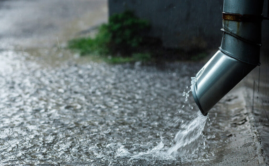 Regen läuft aus Fallrohr auf das Erdreich, statt in einen Erdtank zum Regenwasser sammeln