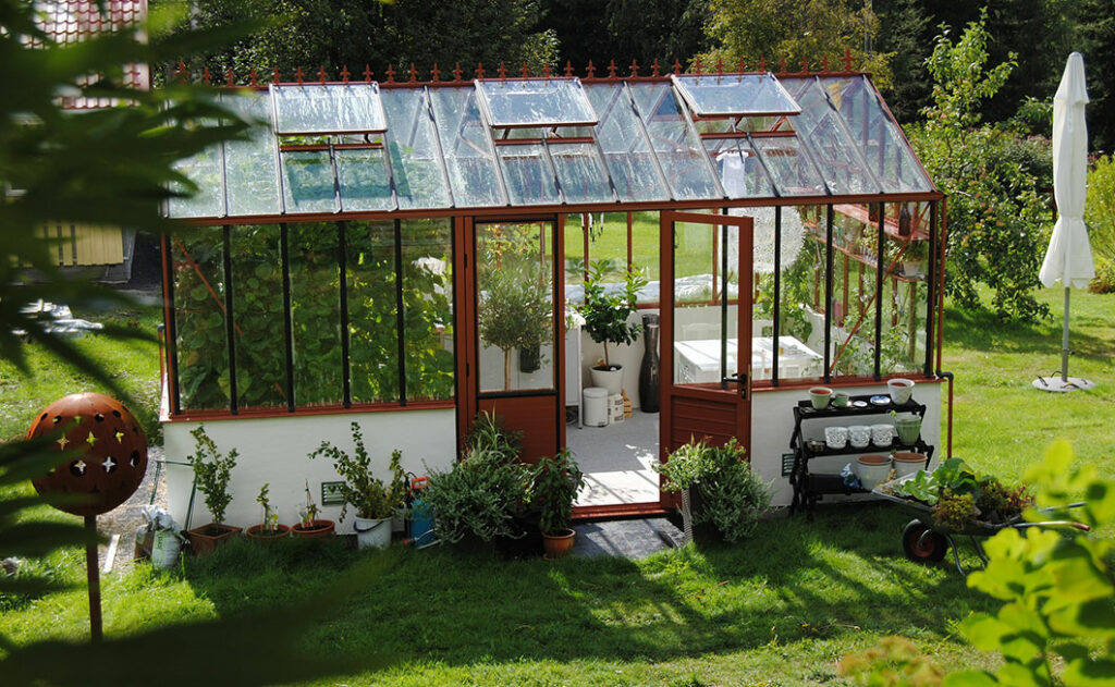 Jolie serre en verre dans un beau jardin verdoyant