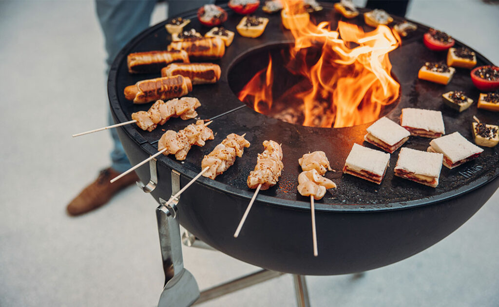 Grill-Feuerschale mit Plancha mit Feuer und Grillspiessen und Gemüse