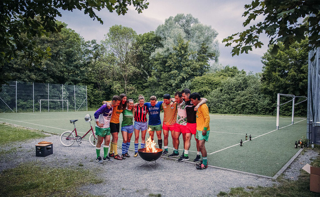 Junge Fussballmanschaft mit BOWL57 vor Fussballfeld auf Kiesplatz