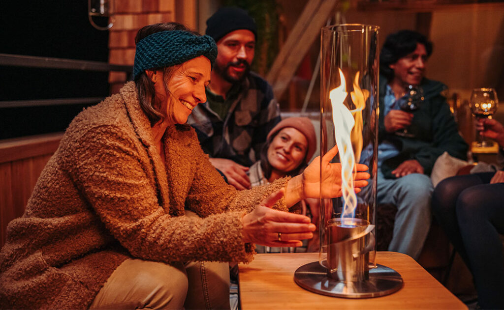 SPIN 1200 eine Frau hält sich ihr Hände zum Wärmen in die Nähe des Tischfeuers