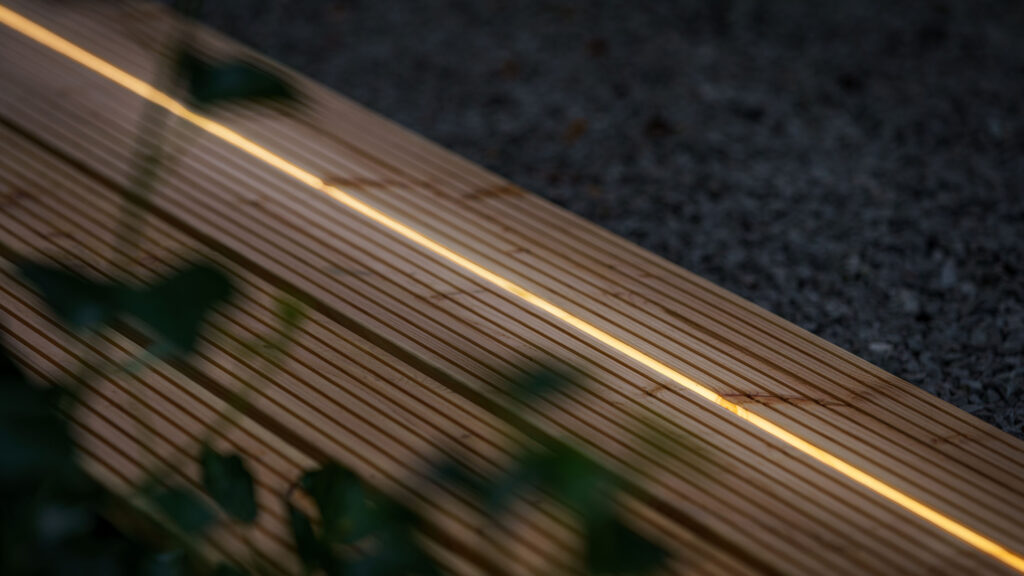 Warmweisser Leuchtstreifen, bündig in eine Holzterrasse im Garten eingelassen.